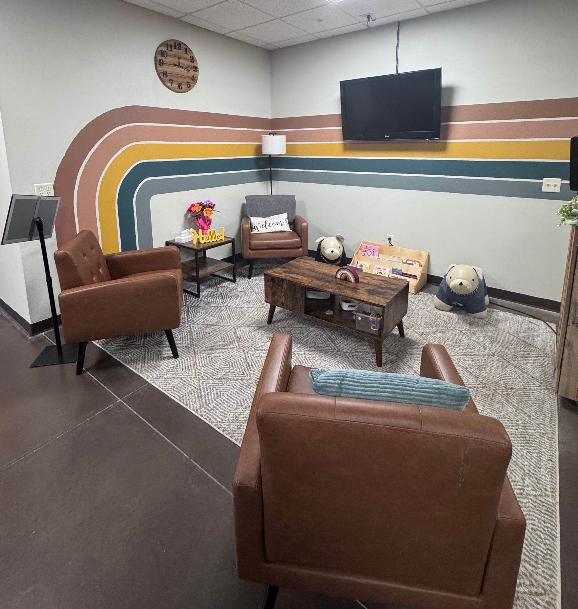 A waiting area featuring brown armchairs, a coffee table, and a colorful arched mural on the wall.