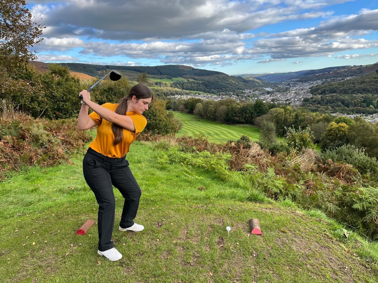 A woman is swinging a golf club on a golf course.