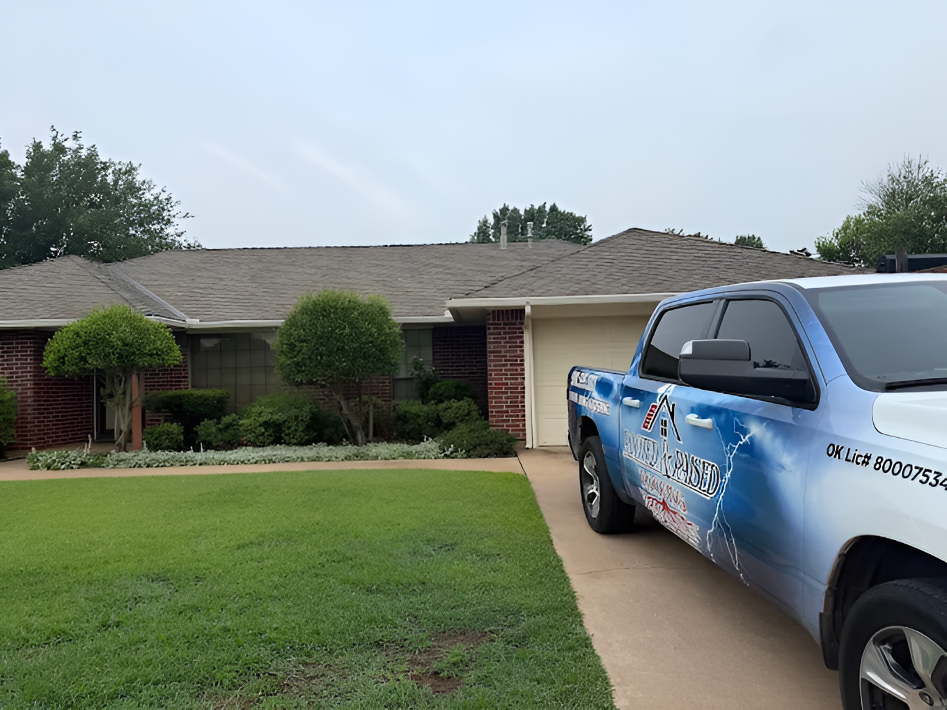 Blue service truck parked by a single-story brick house with a green lawn and trimmed shrubs.