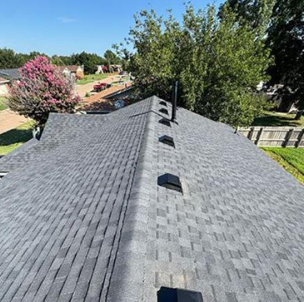 Roof with gray shingles and black vents, viewed from above in a sunny suburban neighborhood