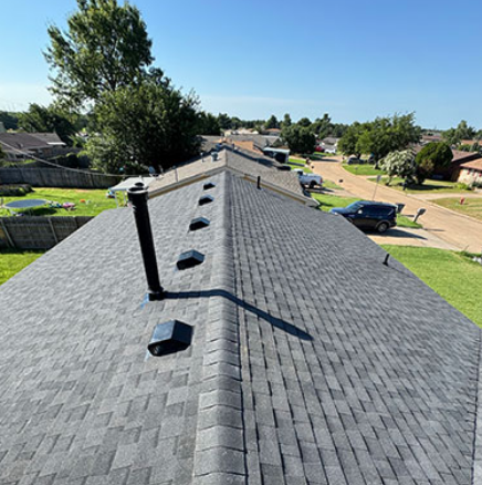 Rooftop with gray shingles and vents overlooking a suburban neighborhood on a clear day