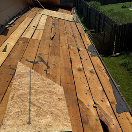 Damaged wooden roof deck with missing boards and exposed underlayment beside a backyard fence
