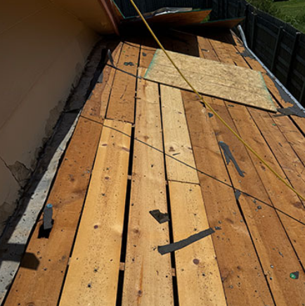 Damaged wooden roof deck with loose boards and debris beside a house wall