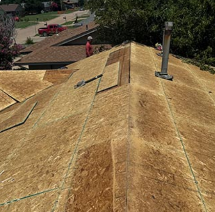 Roof under repair with exposed plywood sheathing and a chimney, viewed from above.