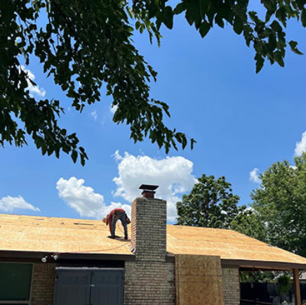 Worker on a roof replacing shingles on a house under a bright blue sky
