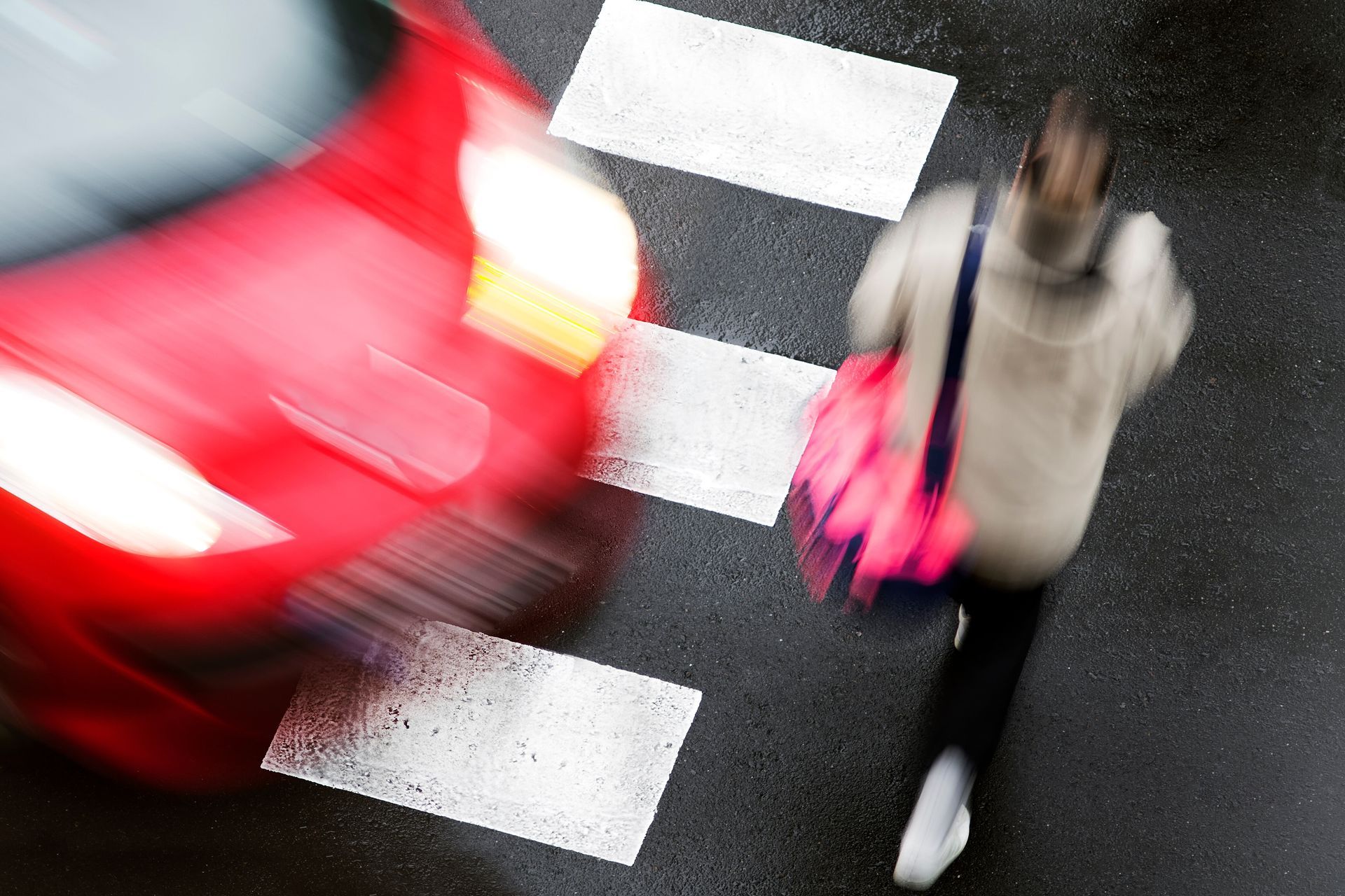 A blurry picture of a person crossing a street with a red car behind them