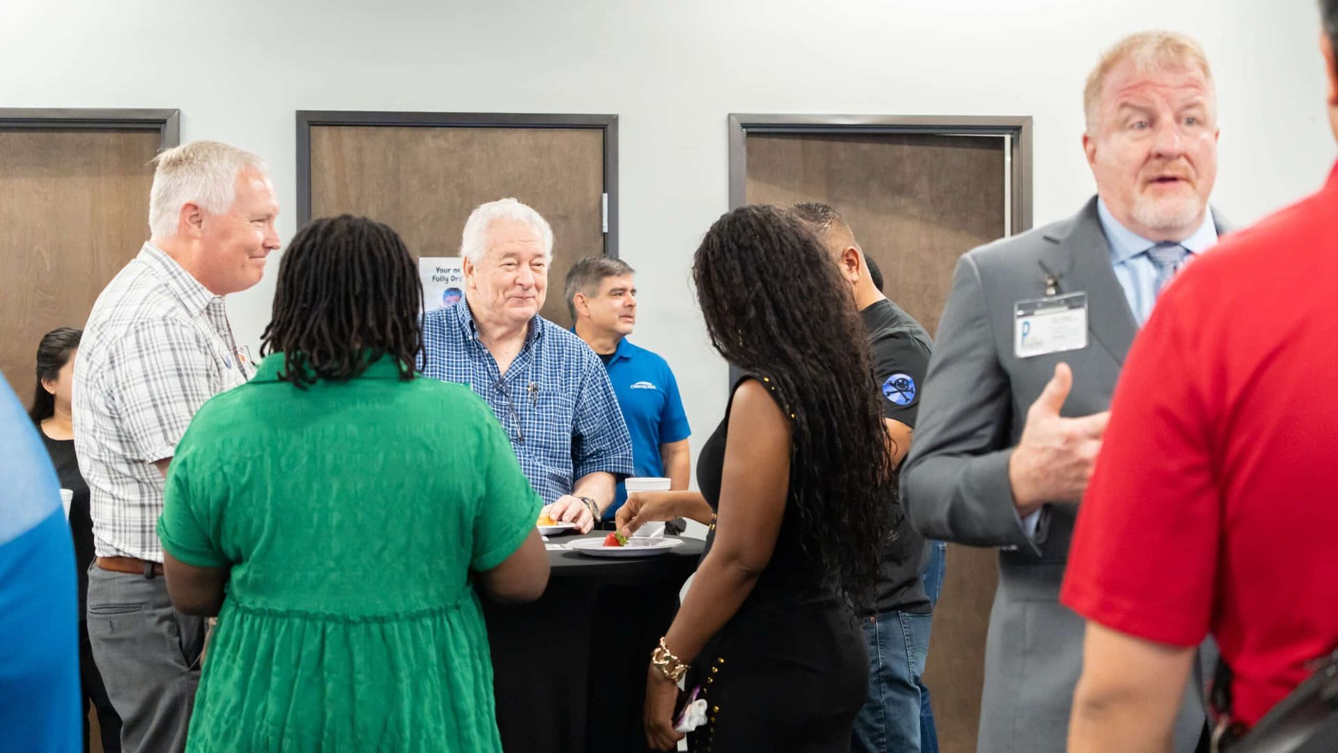 People talking at an indoor networking event, with several adults standing around a table.