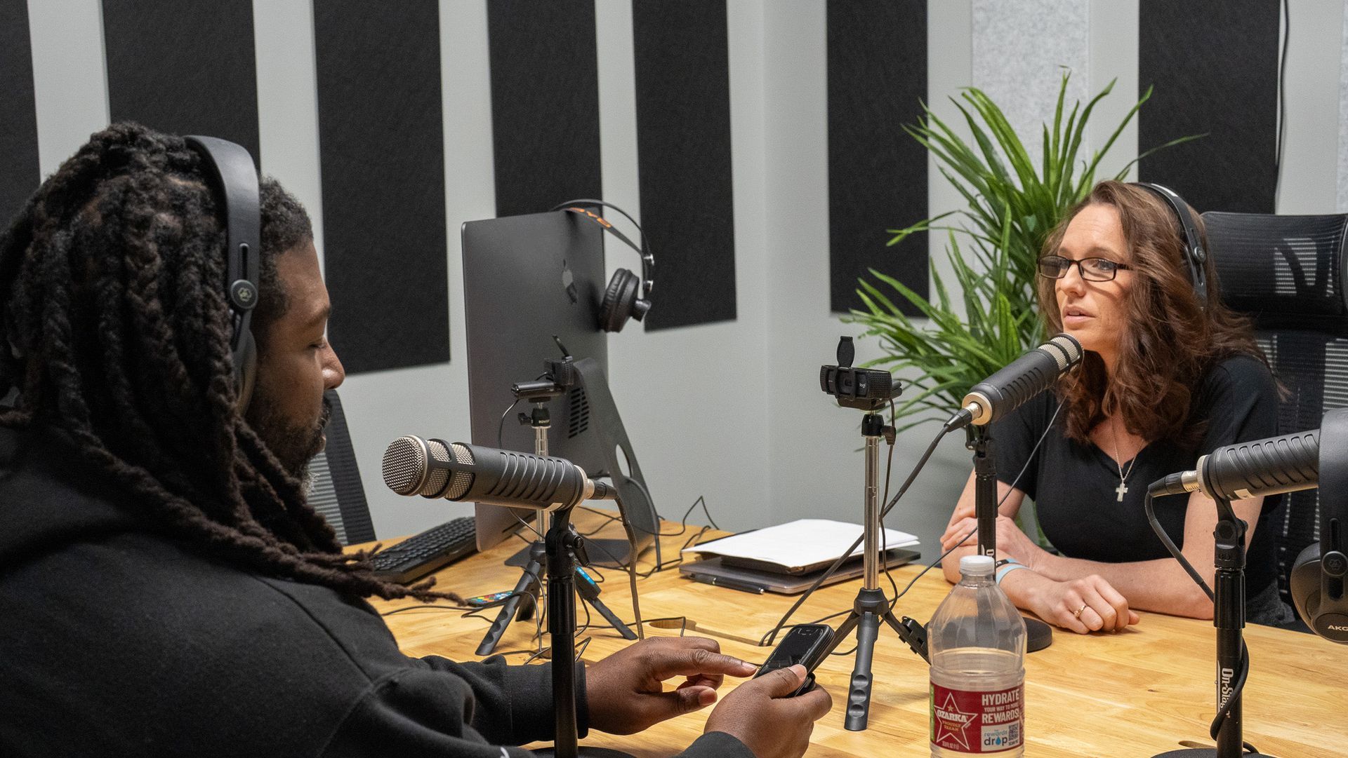 Two people recording a podcast in a studio, seated across from each other with microphones.