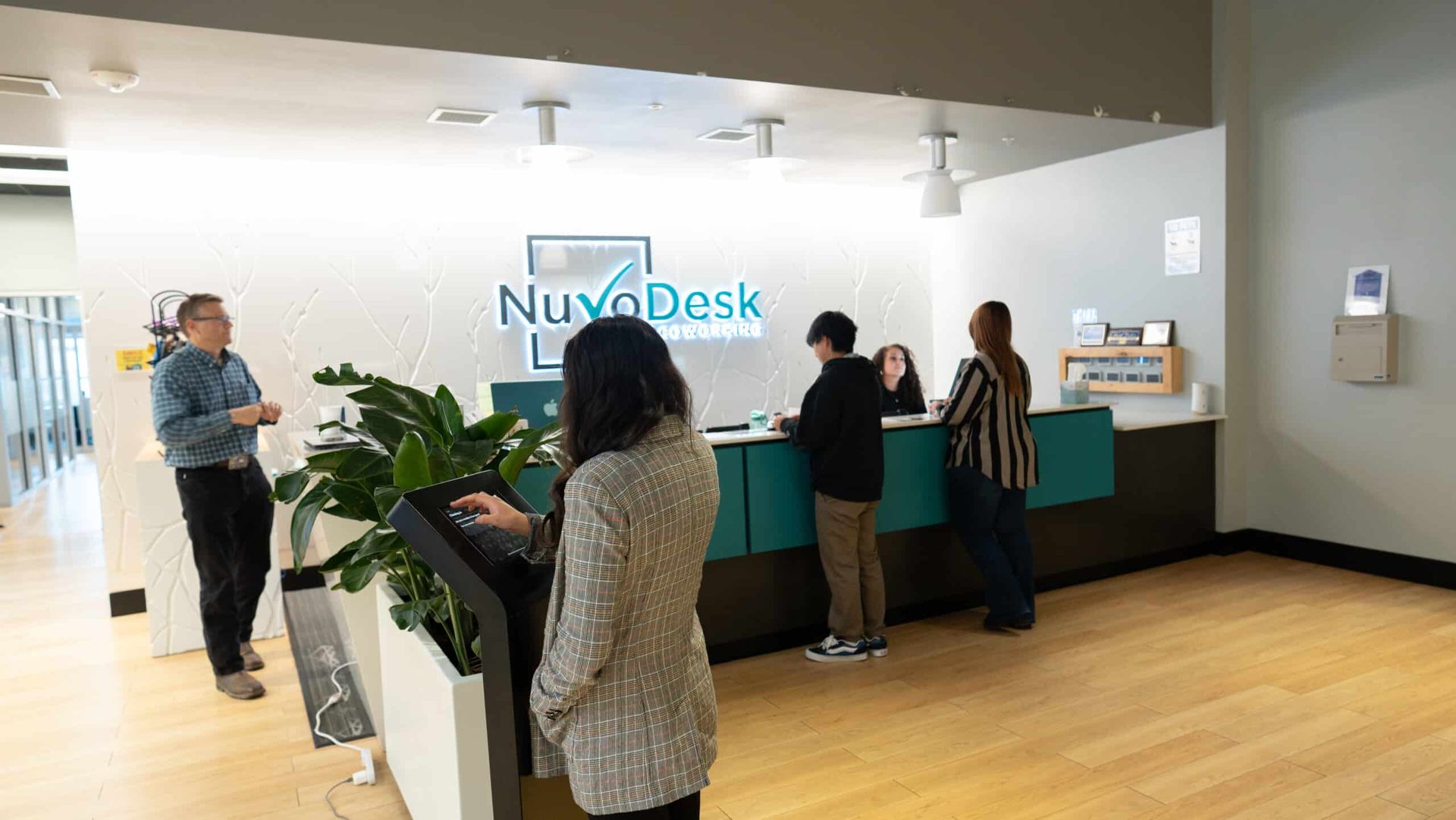 People standing at a NuvoDesk reception counter in a bright lobby.