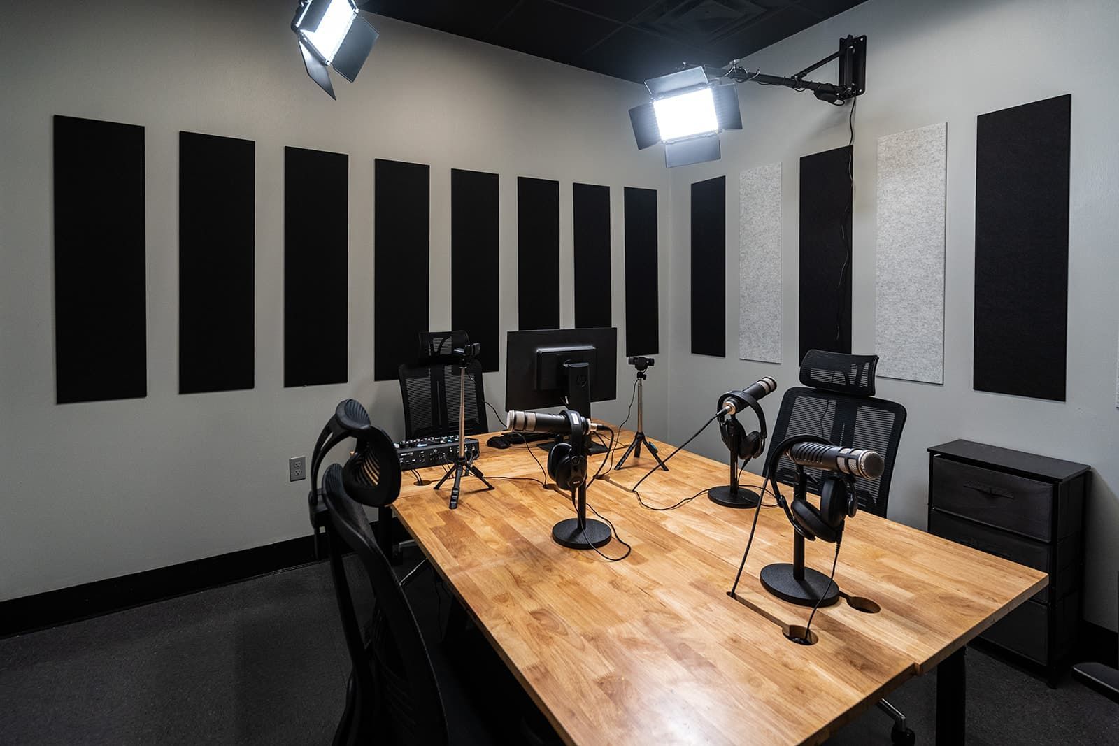 Podcast recording studio with black acoustic panels, microphones, headphones, and chairs around a wooden table