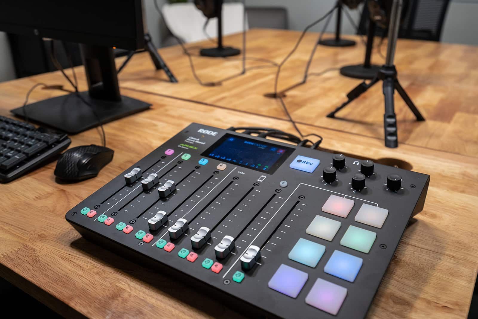 Audio mixing console with sliders, knobs, and illuminated pads on a wooden desk in a studio.