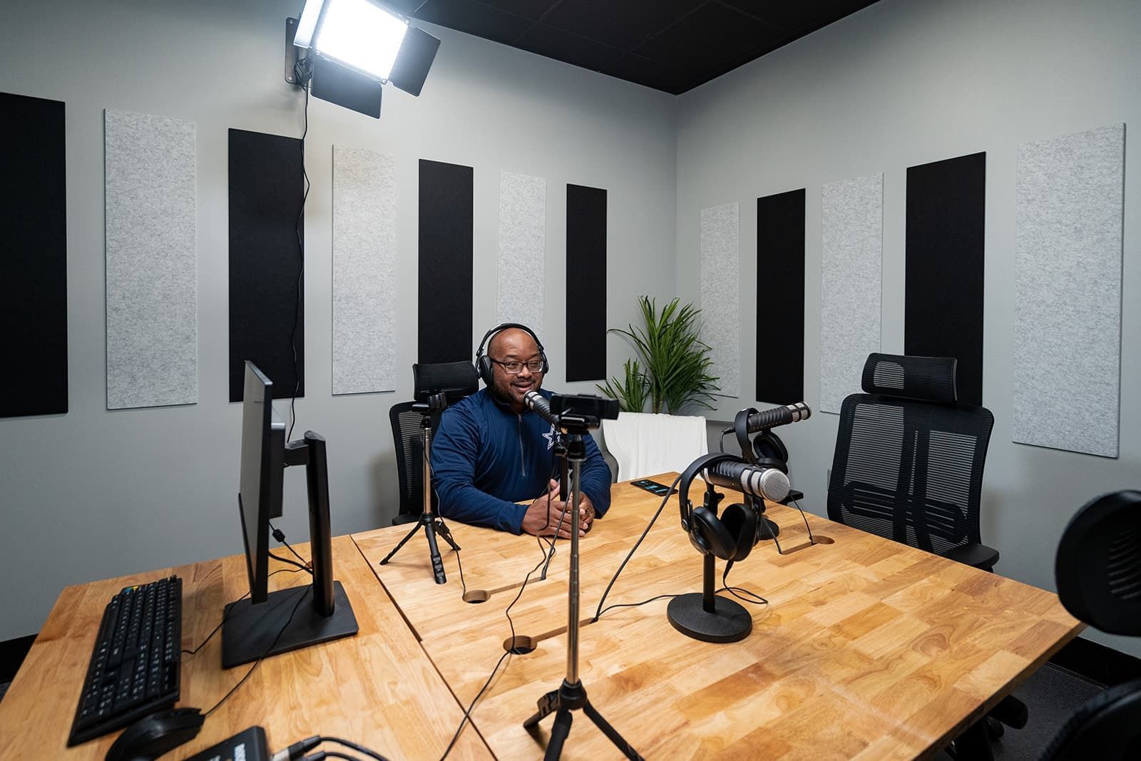 Person speaking into a microphone in a modern podcast studio with sound panels and recording equipment