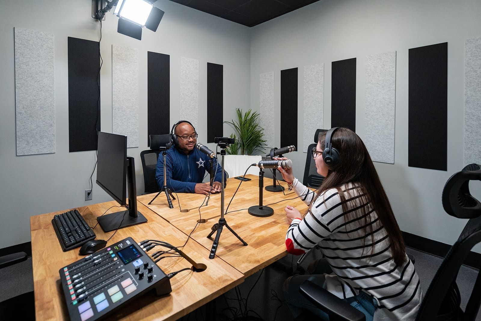 Two people recording a podcast in a studio with microphones, headphones, and audio equipment.