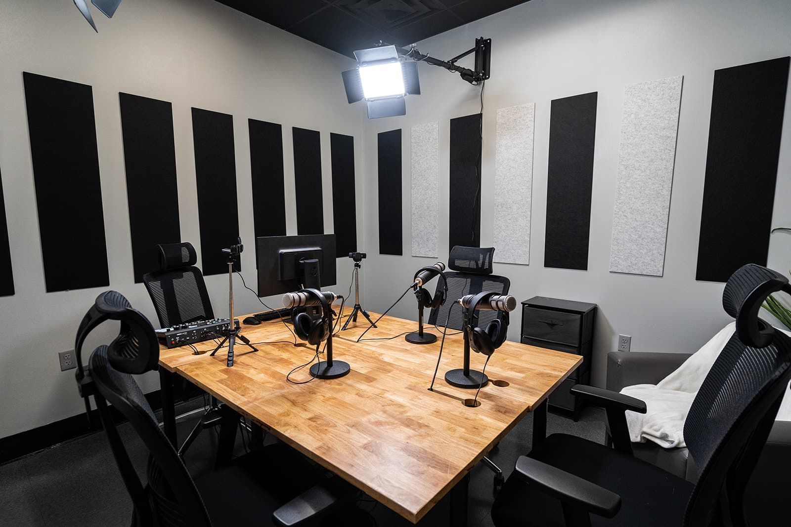 Podcast studio with black chairs, microphones, and acoustic panels around a wooden table