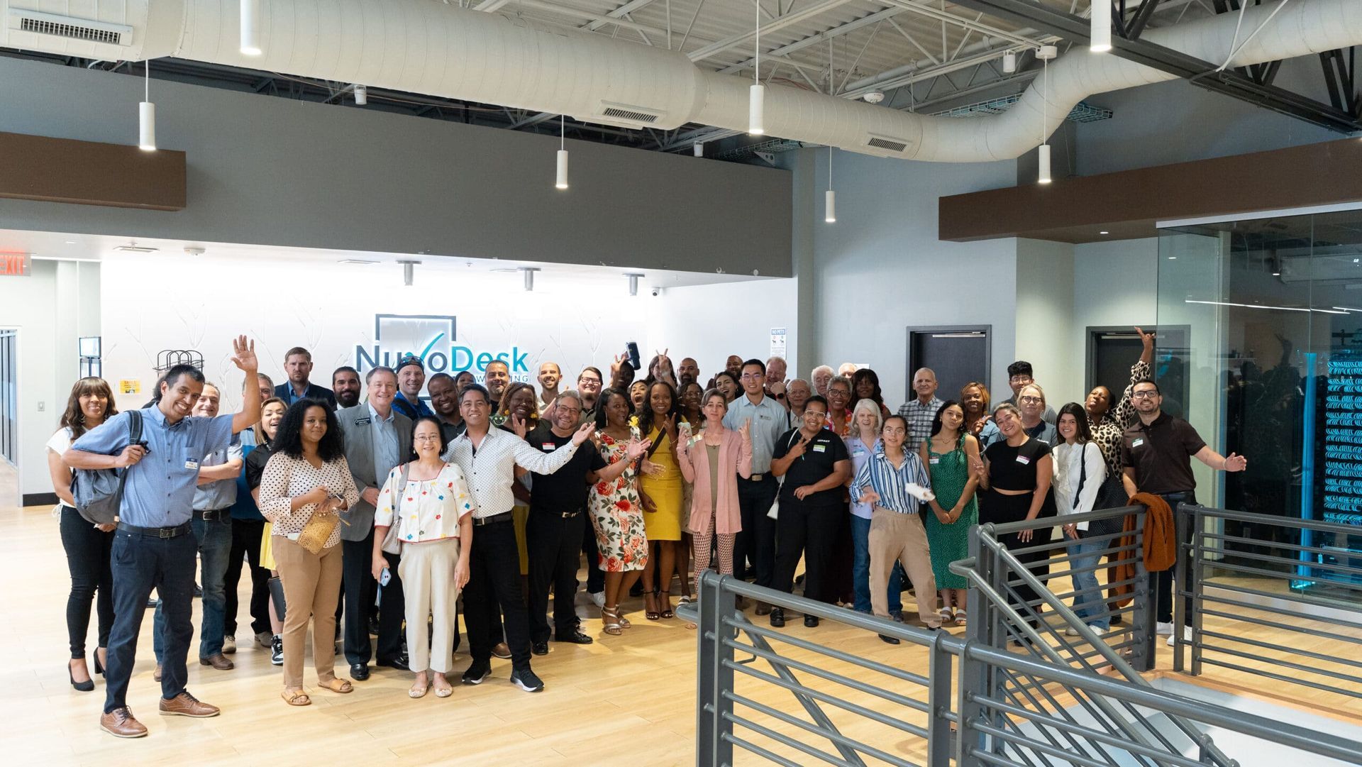 Large group posing in a bright office lobby, smiling and waving for a group photo