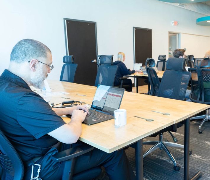 Person working on a laptop in a modern office meeting room with tables and chairs