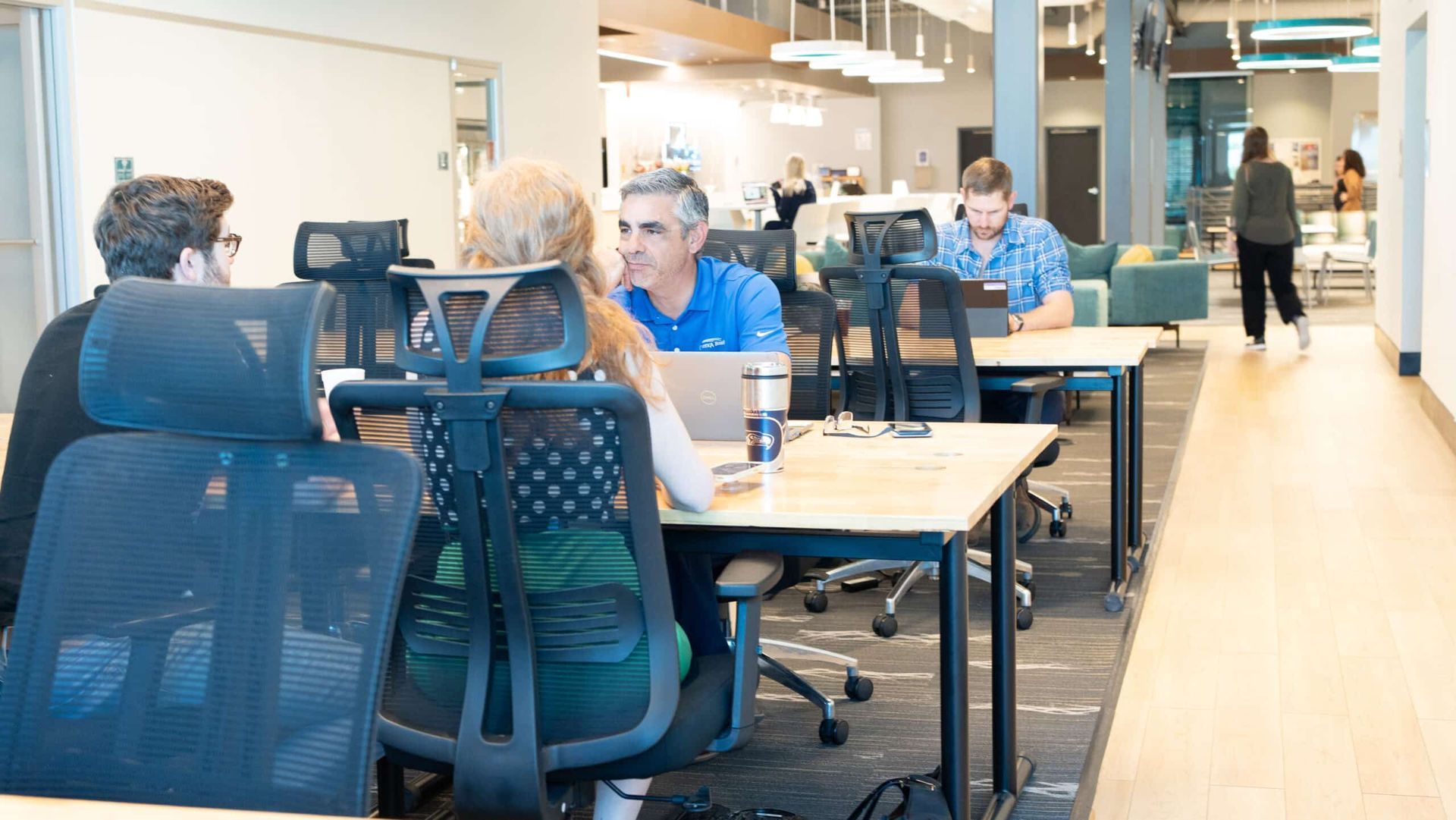 People seated at desks in a bright shared workspace, with laptops and office chairs.
