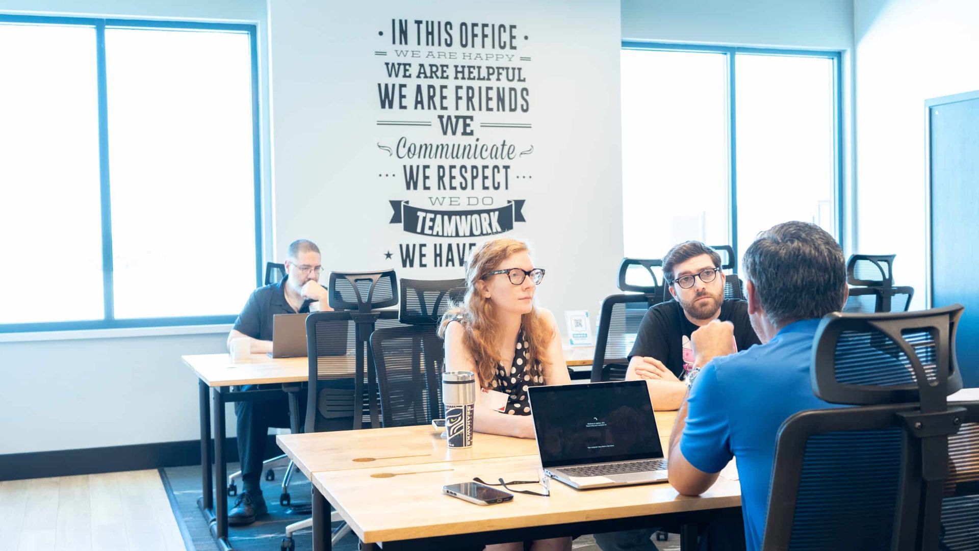 Coworking office with people meeting at a table near large windows and laptops