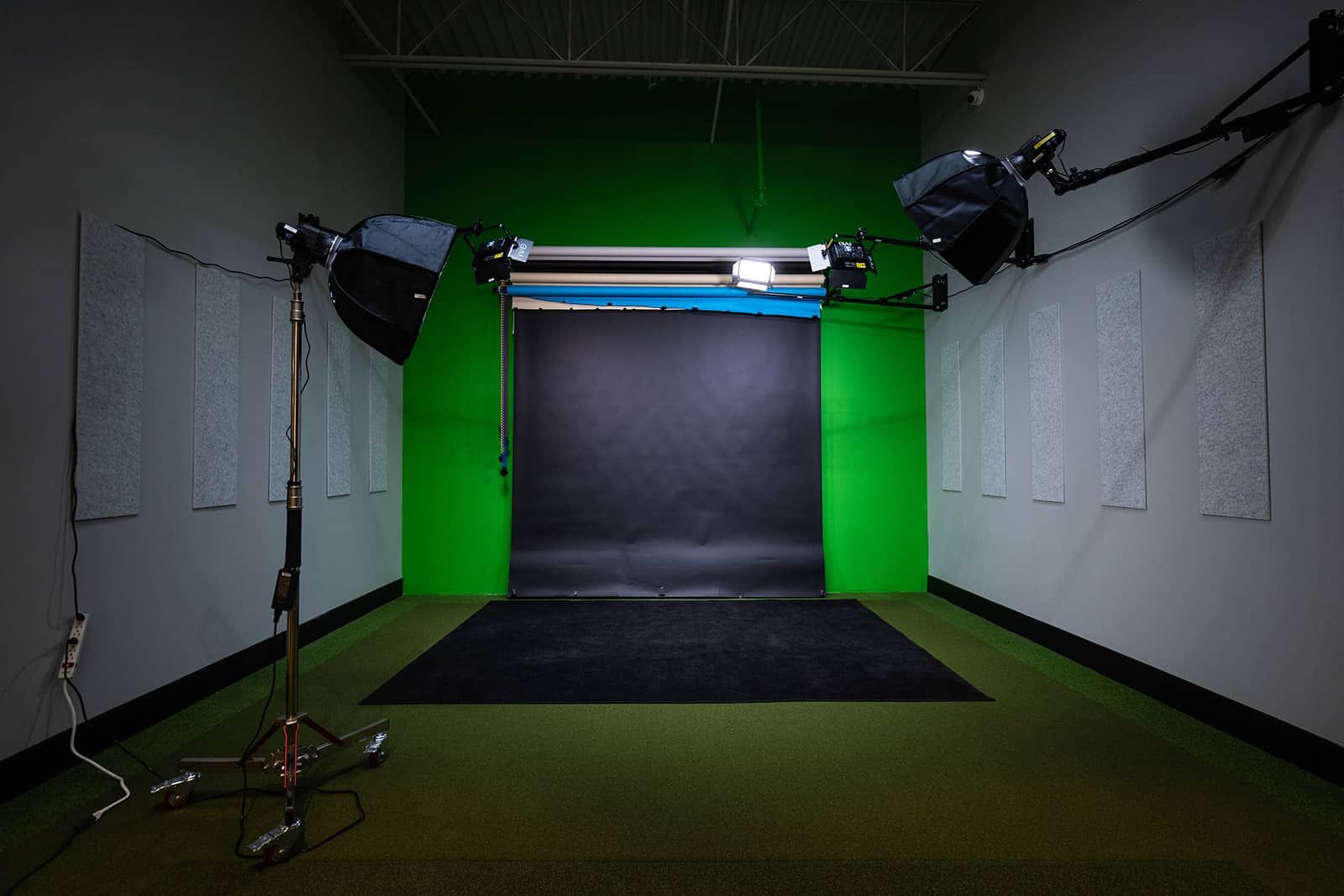 Empty studio with green screen backdrop, lighting equipment, and black floor mat.