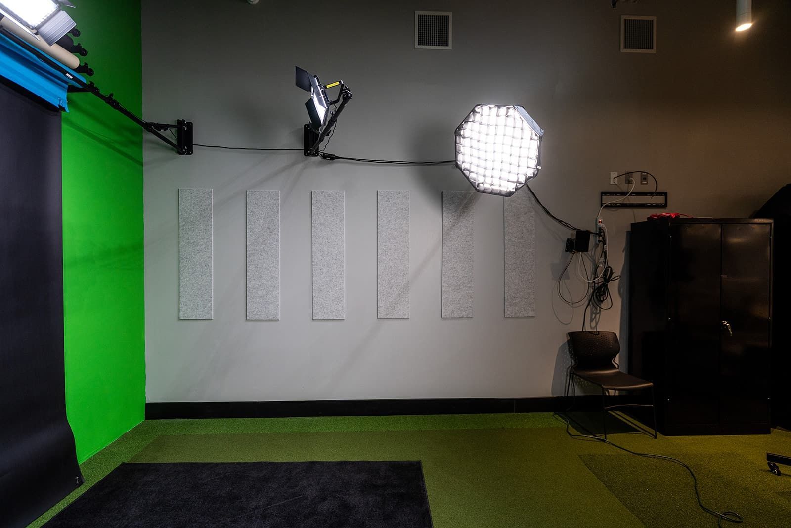 Empty photo studio with green screen, softbox lights, and black backdrops on a carpeted floor