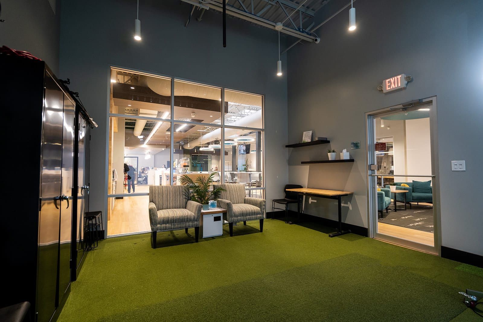 Office lounge with green turf carpet, glass meeting room, desks, and hanging lights