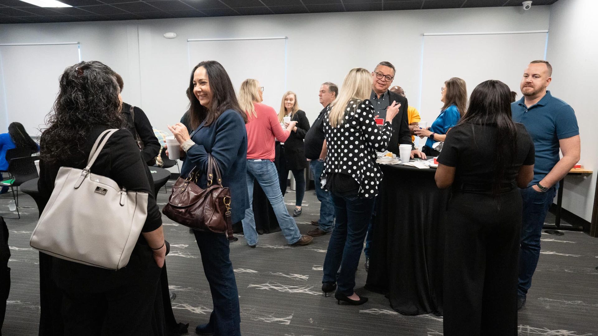 People mingling at a networking event in a conference room, with drinks and small tables.