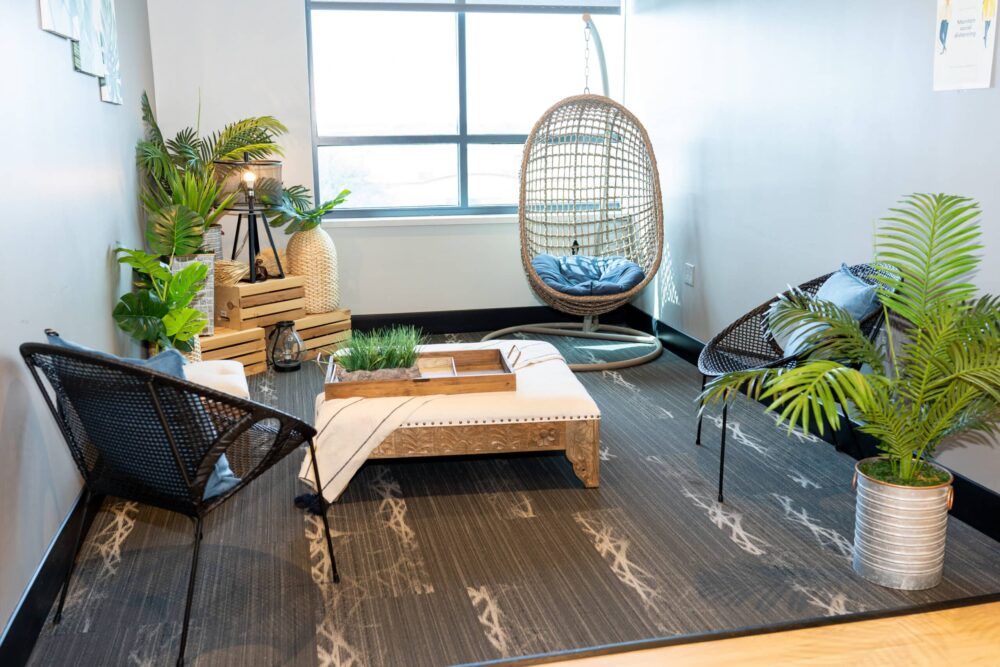 Modern lounge with black chairs, low wooden table, hanging egg chair, and potted plants by a bright window