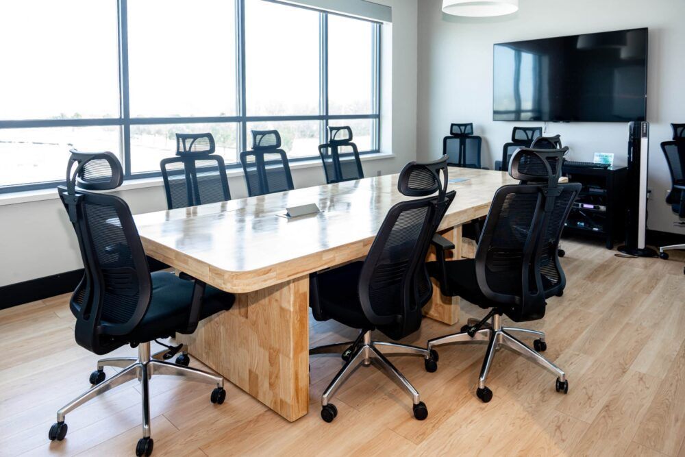 Modern conference room with a wooden table, black office chairs, and a wall-mounted TV