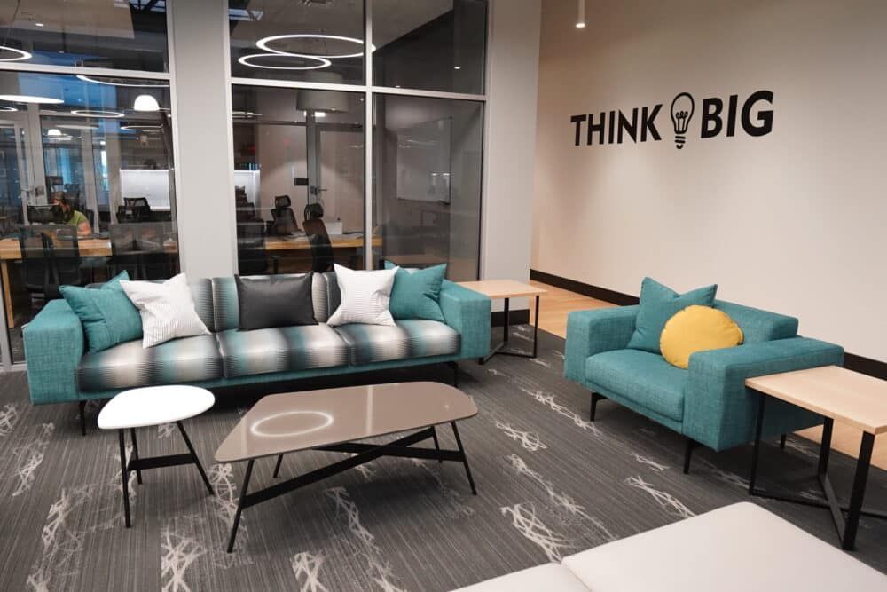 Modern office lounge with teal sofas, coffee tables, and a “THINK BIG” wall sign