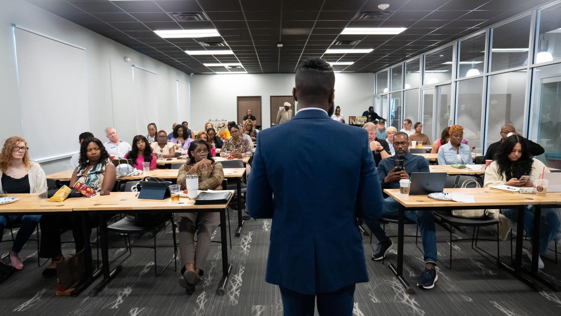 Presenter facing a seated audience in a bright conference room during a meeting or lecture