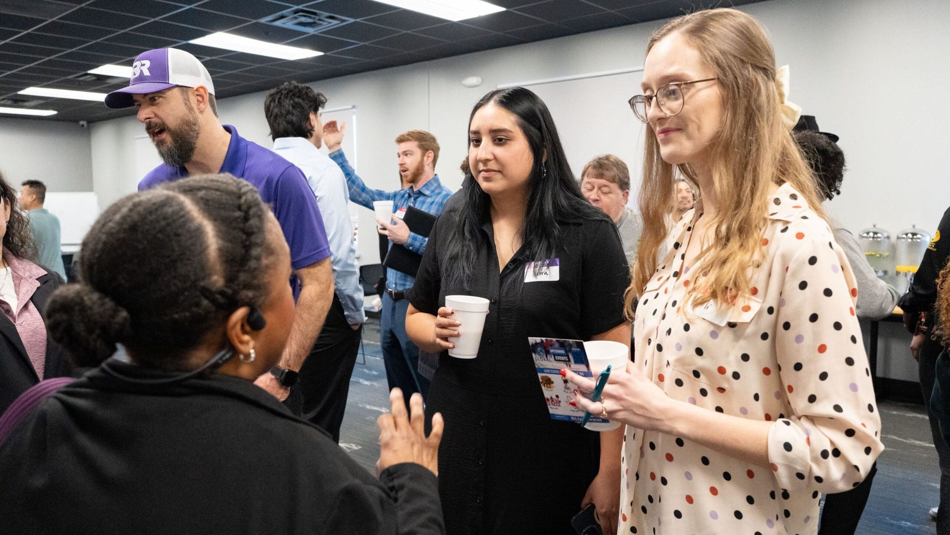 People talking at a crowded indoor networking event, holding drinks and badges.
