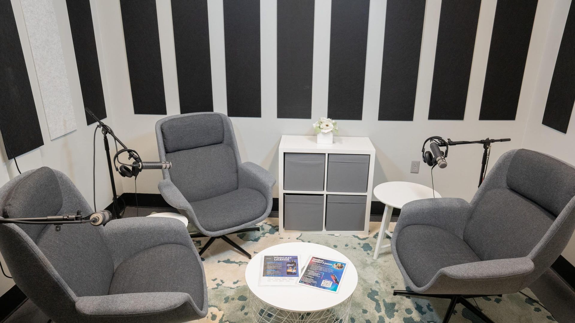 Small lounge with gray chairs, white side table, black-and-white striped wall, and a round rug with magazines.