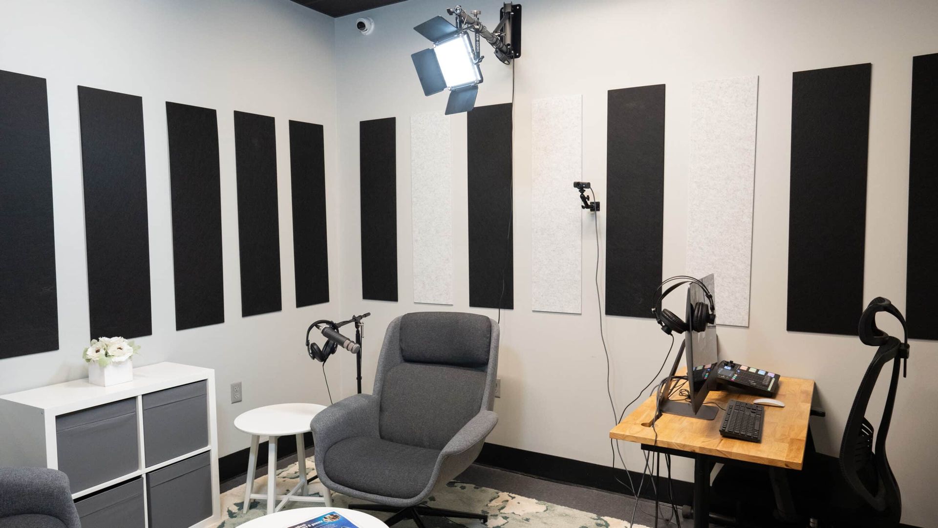Small recording studio with acoustic foam panels, chair, desk, and studio lights.