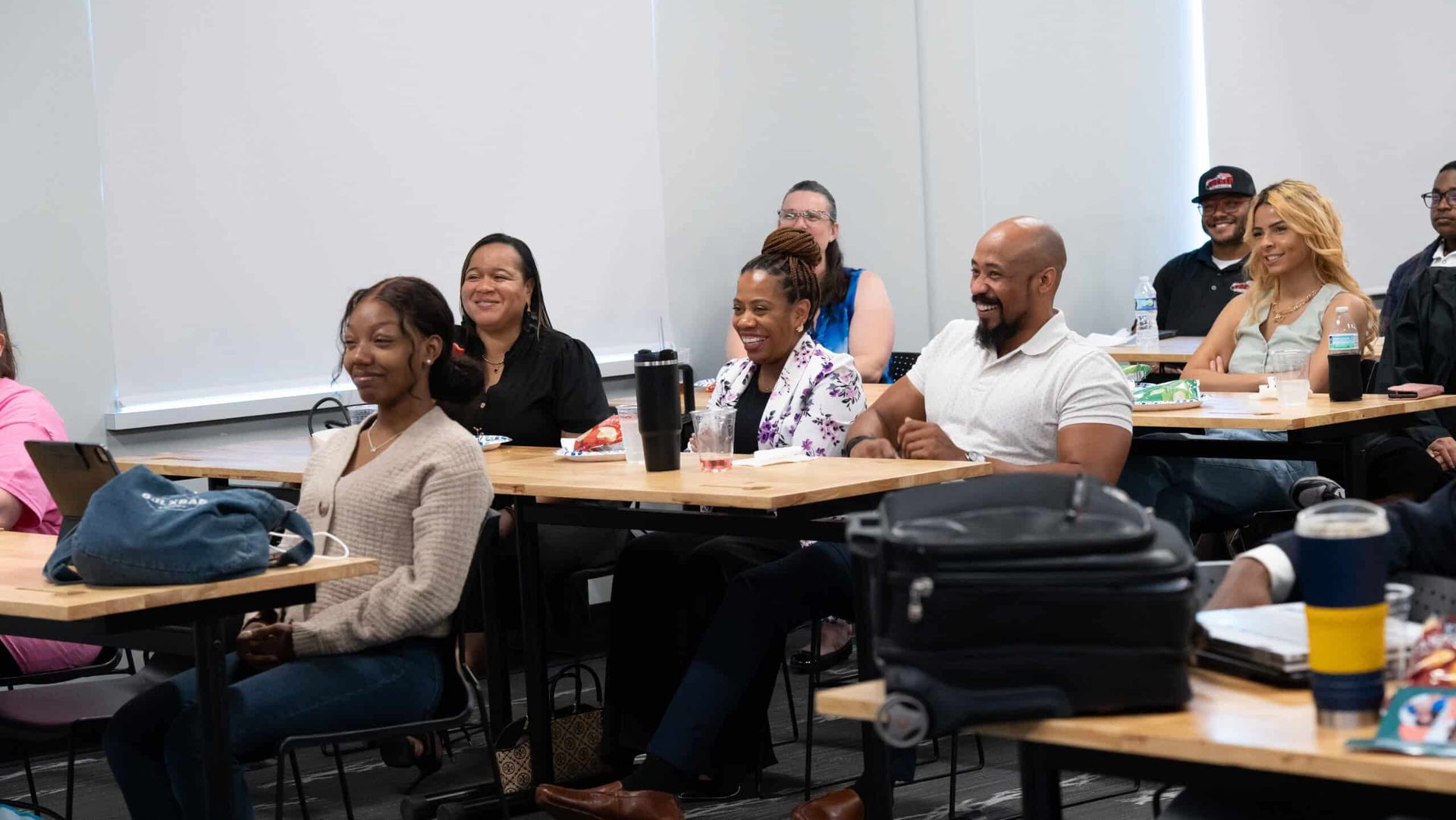 People seated at desks in a classroom, smiling and listening during a lesson.