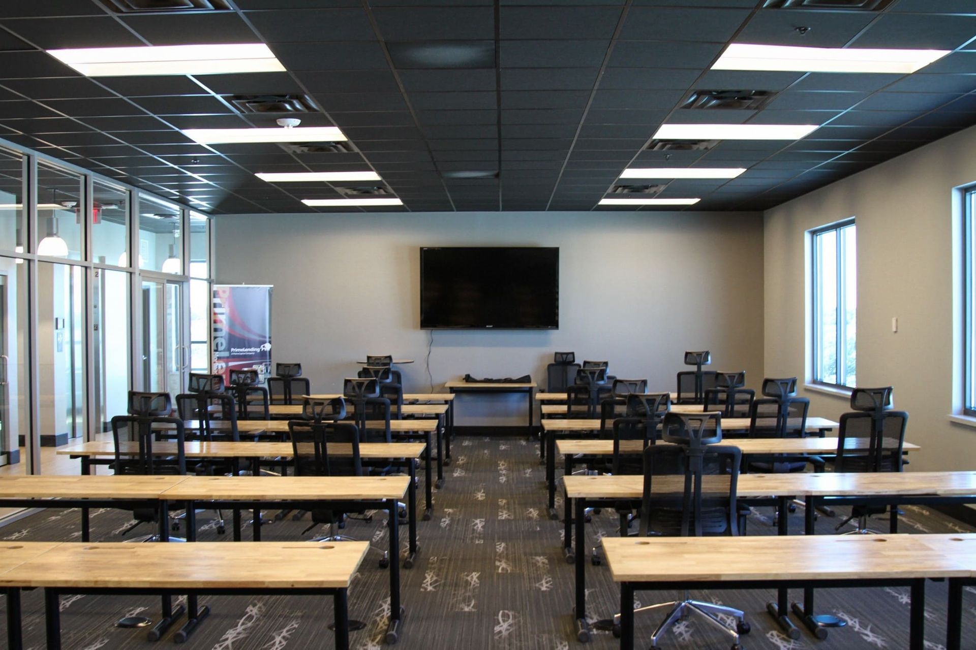 Empty classroom with rows of tables and chairs facing a wall-mounted screen