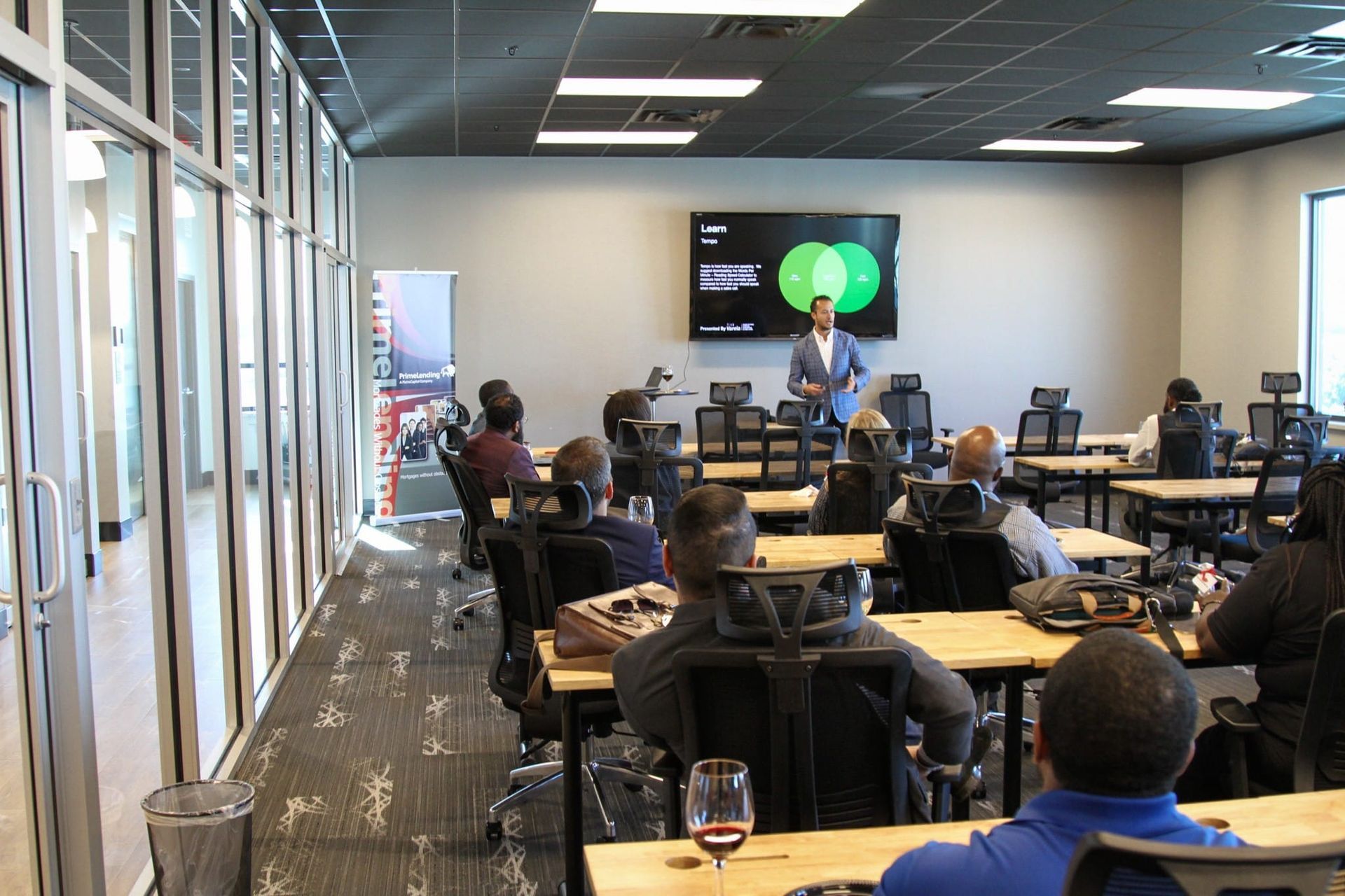 Conference room training session with people seated at tables watching a presenter on a screen