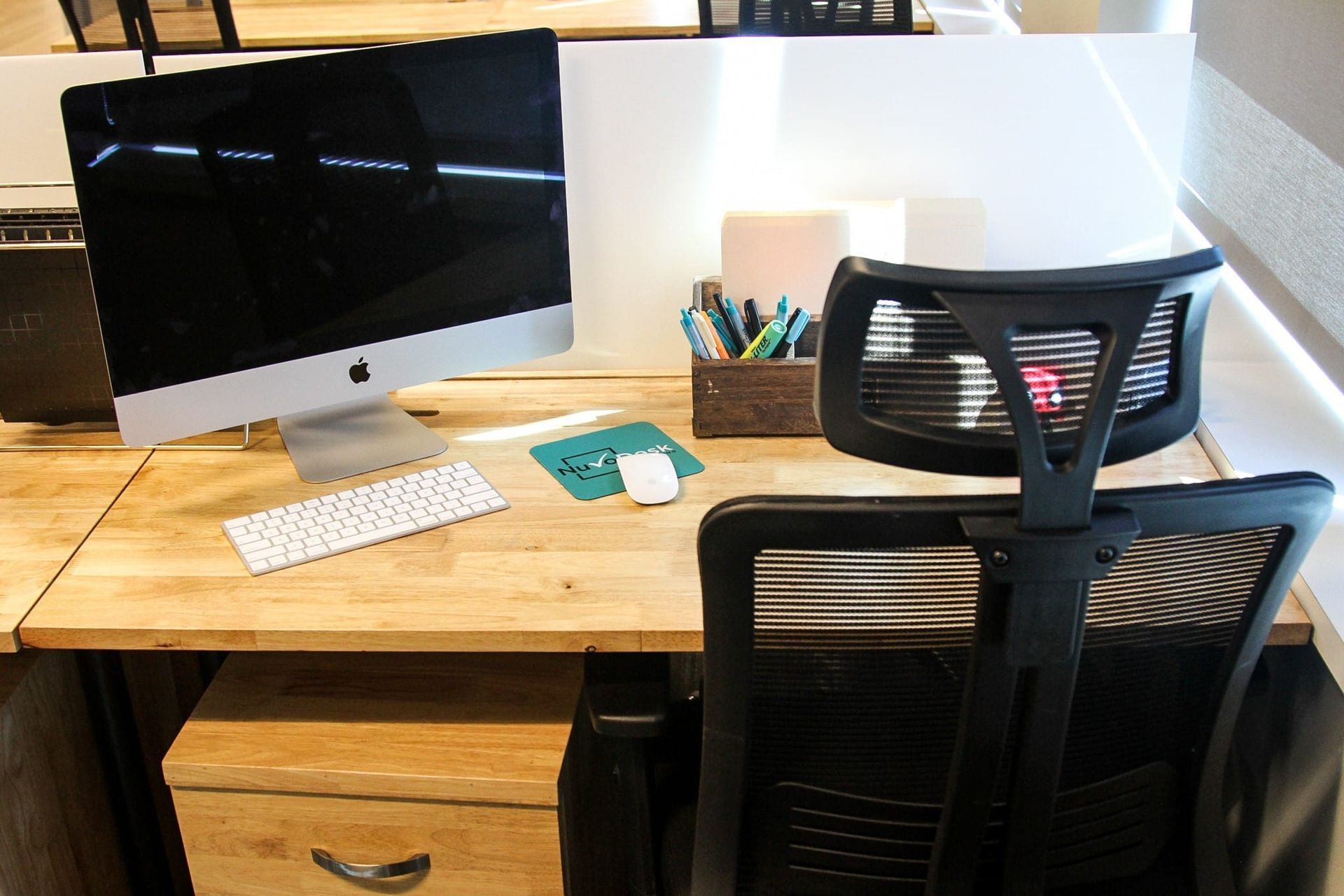 Desk workspace with iMac, keyboard, mouse, notebooks, and a black office chair