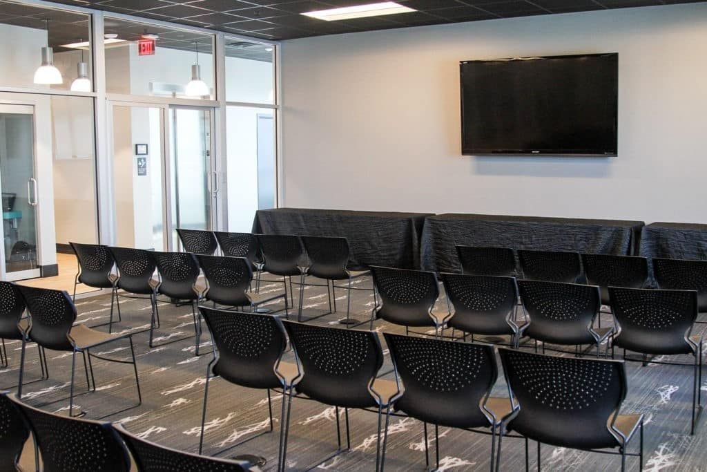 Empty conference room with rows of black chairs facing a wall-mounted TV screen
