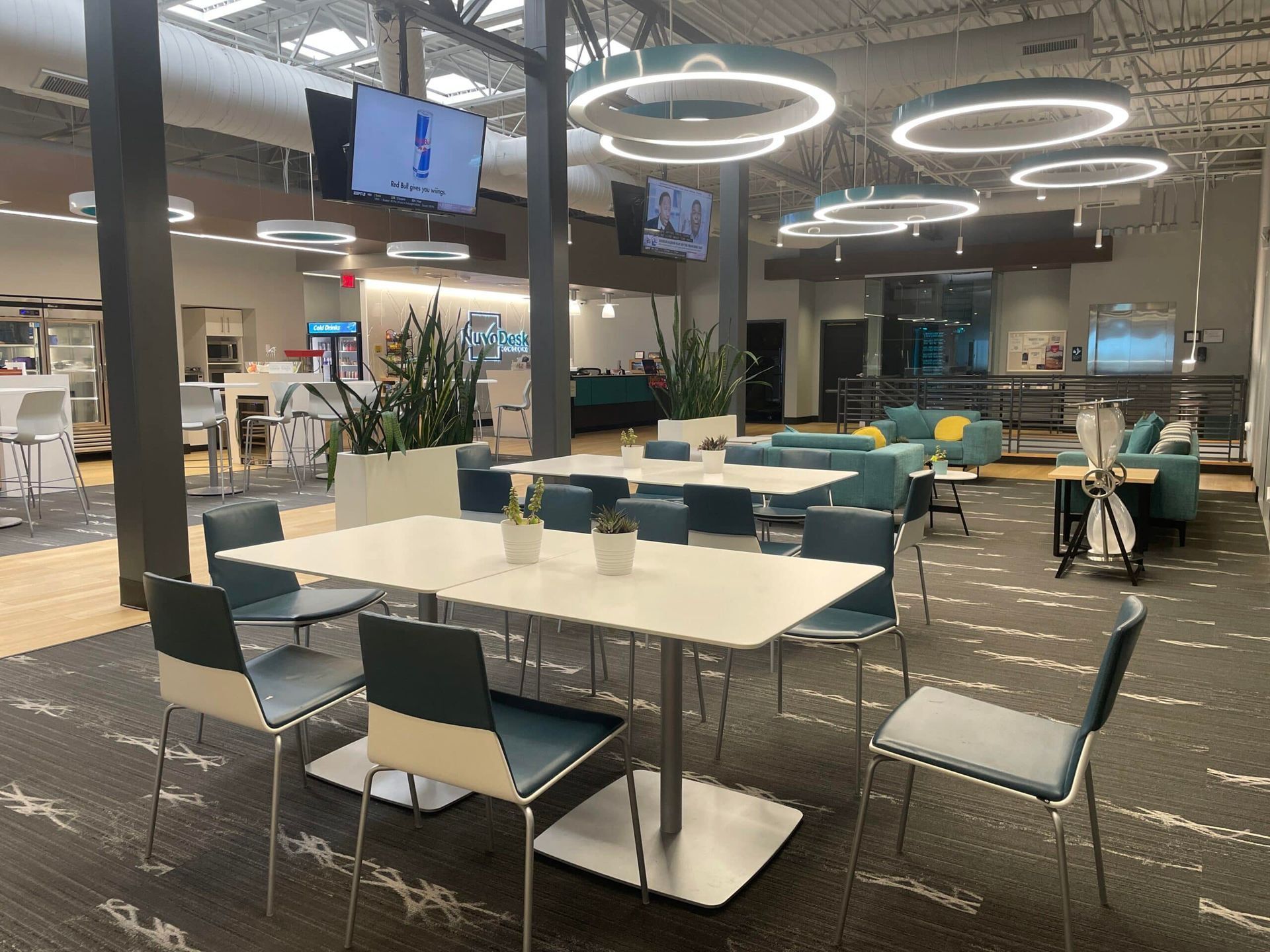 Empty modern cafeteria with tables, chairs, pendant lights, and mounted screens on the ceiling