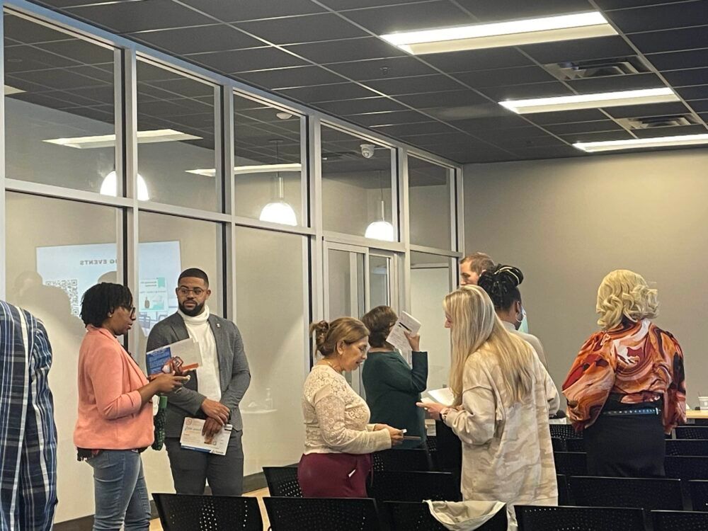 People gathered in a conference room, talking and holding papers around a table.