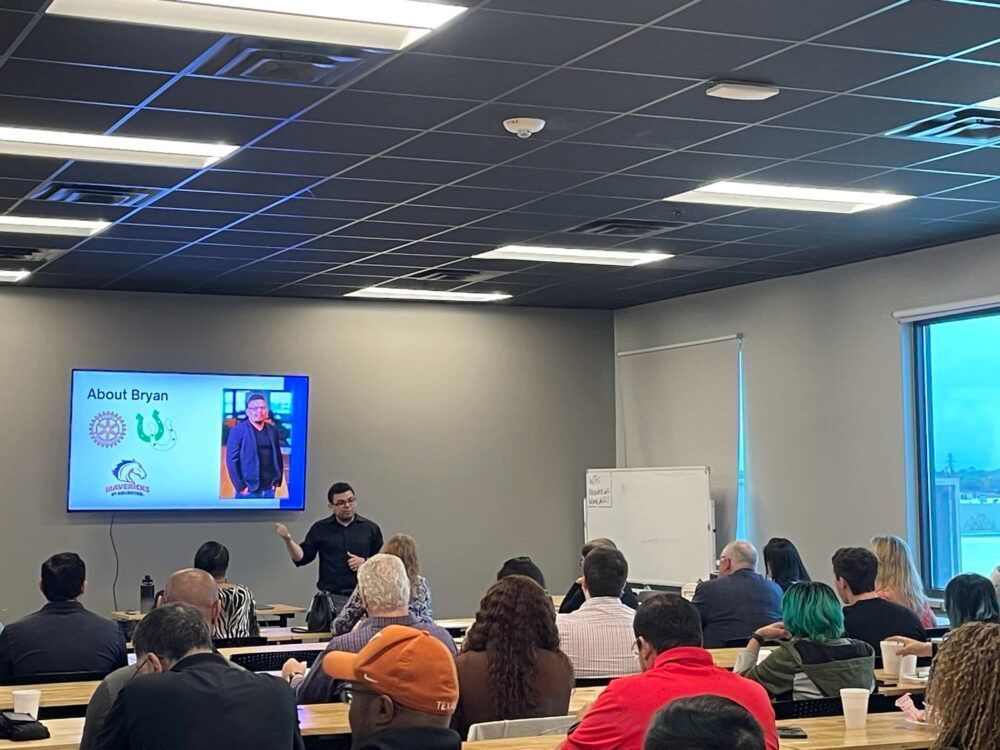 Classroom seminar with audience seated facing a presenter near a wall screen and whiteboard