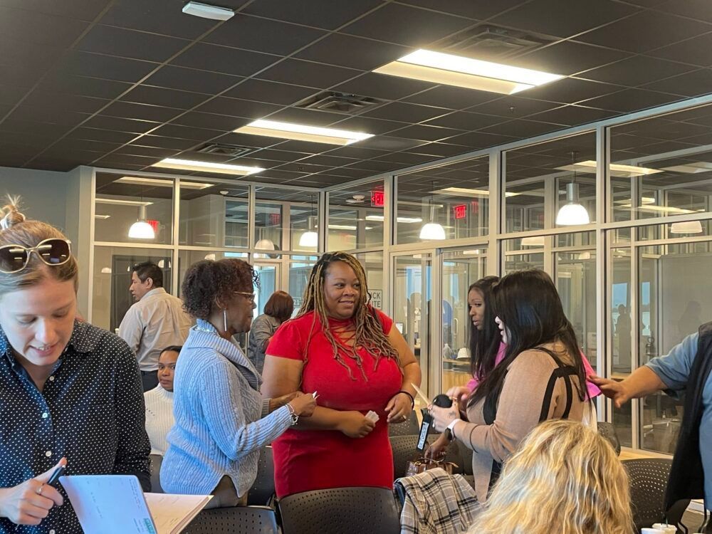 People chatting in a glass-walled office lounge under bright ceiling lights.