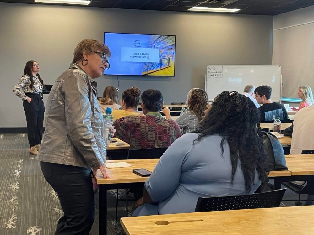 Classroom training session with presenter at front, participants seated at tables, and slides on a screen