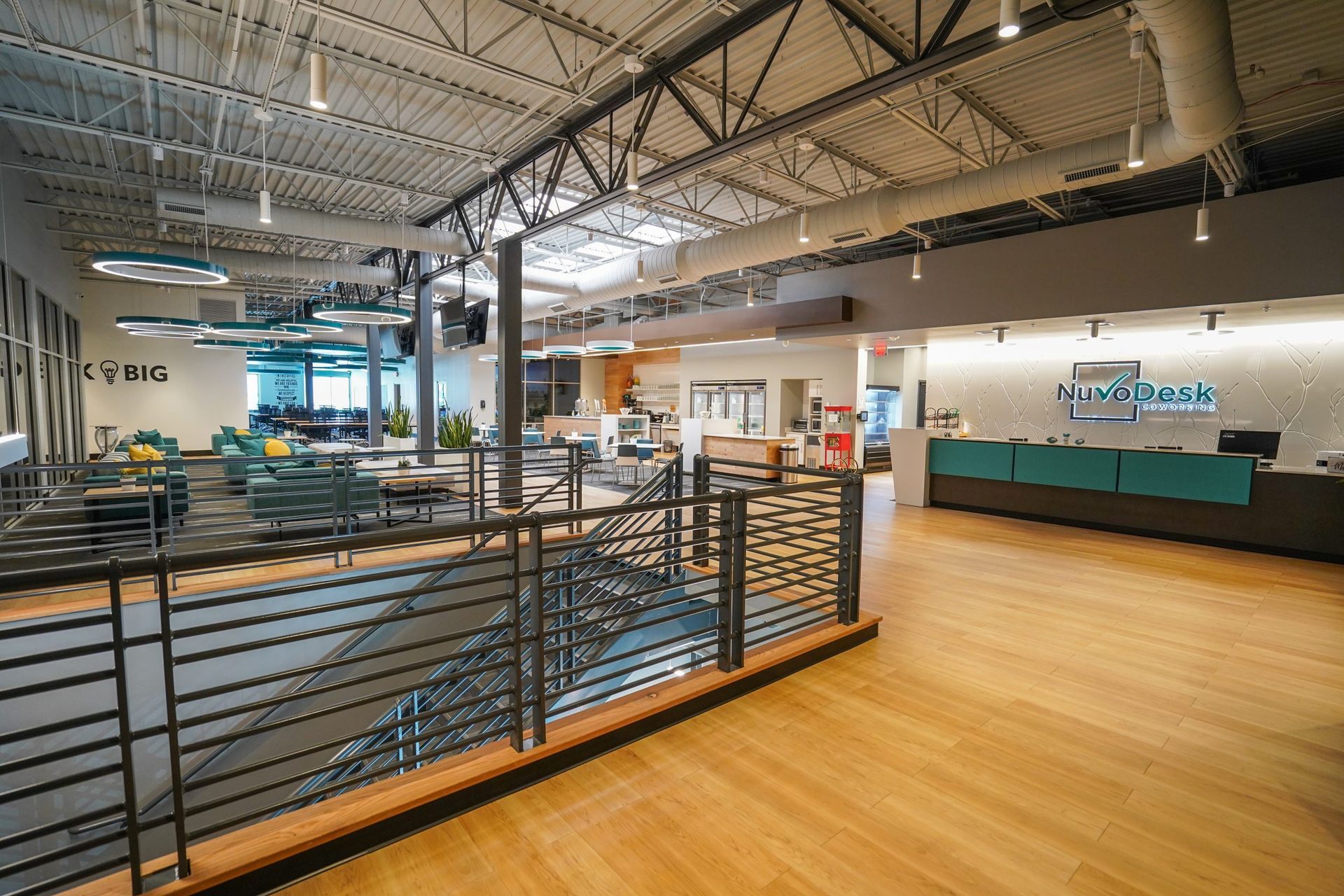 Modern office lobby with wood floor, metal railing, reception desk, and exposed ceiling beams