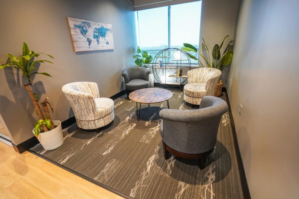 Small office lounge with four chairs, round tables, large window, plants, and world map artwork