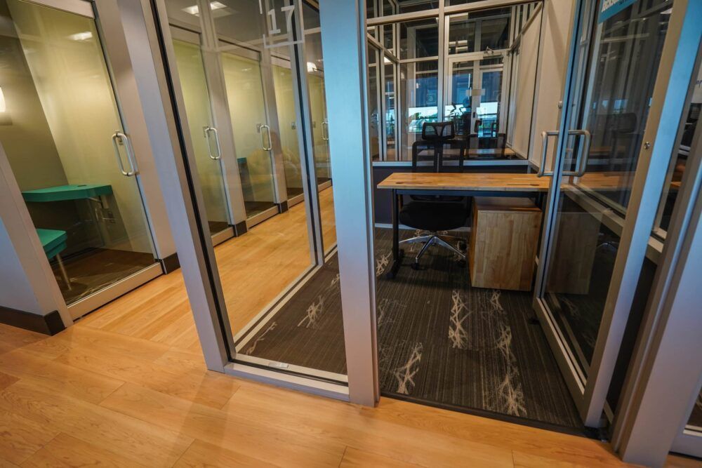 Glass-walled office meeting room with wooden floor and a desk inside