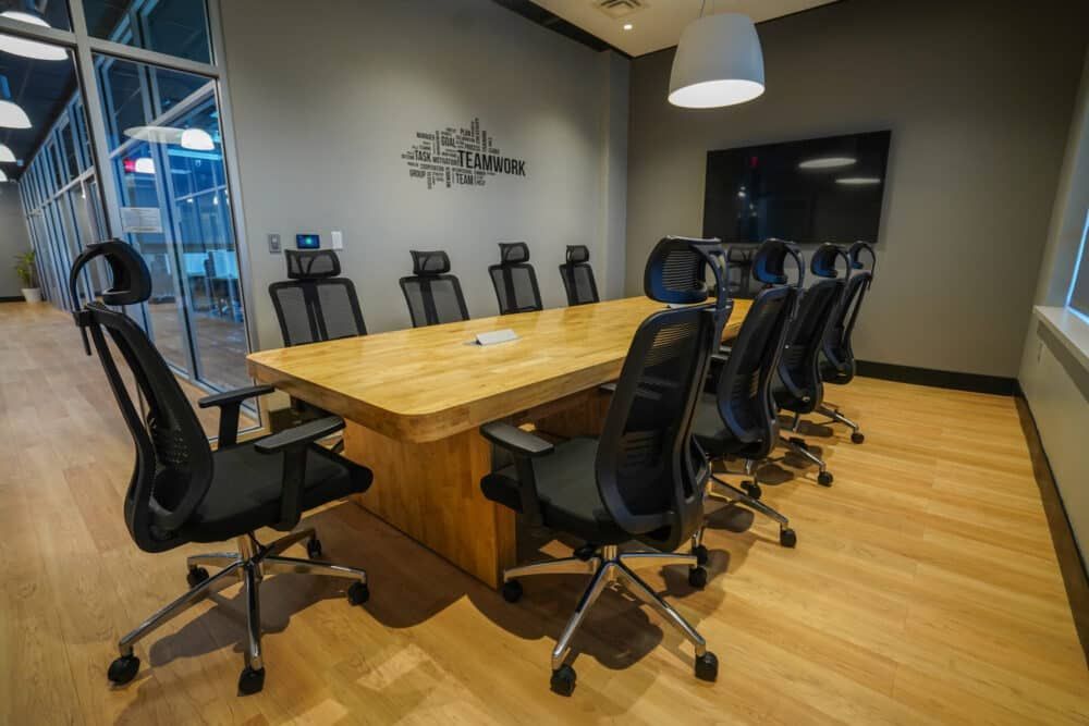 Modern conference room with a long wooden table, black office chairs, and a wall-mounted TV
