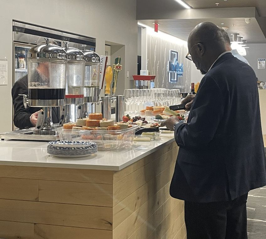 Man selecting food at a buffet counter in a bright cafeteria with trays, drinks, and pastries