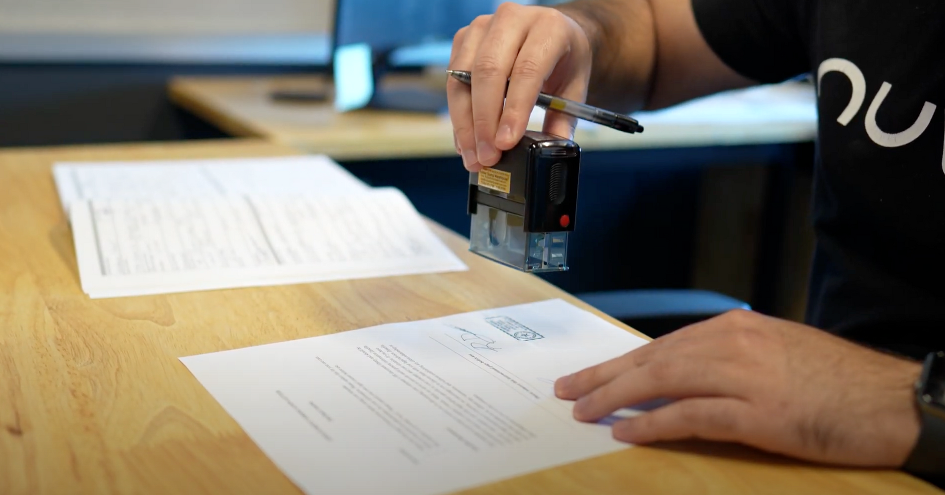 Hands stamping documents on a wooden desk in an office setting