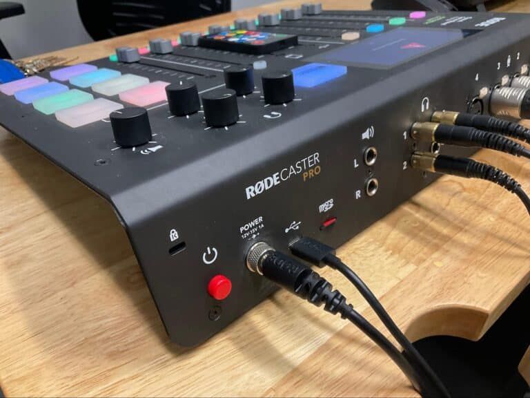 Redcaster audio mixer with colorful pads and knobs on a wooden desk, close-up of connected cables